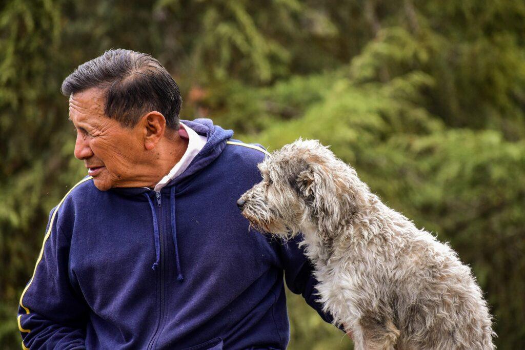 Elderly man gently holding a senior dog outdoors, symbolizing companionship and senior dog care